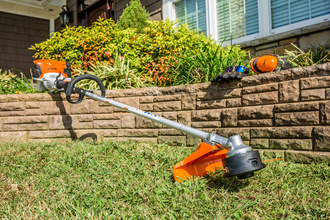Stihl FS 131 R trimming grass next to a stone retaining wall